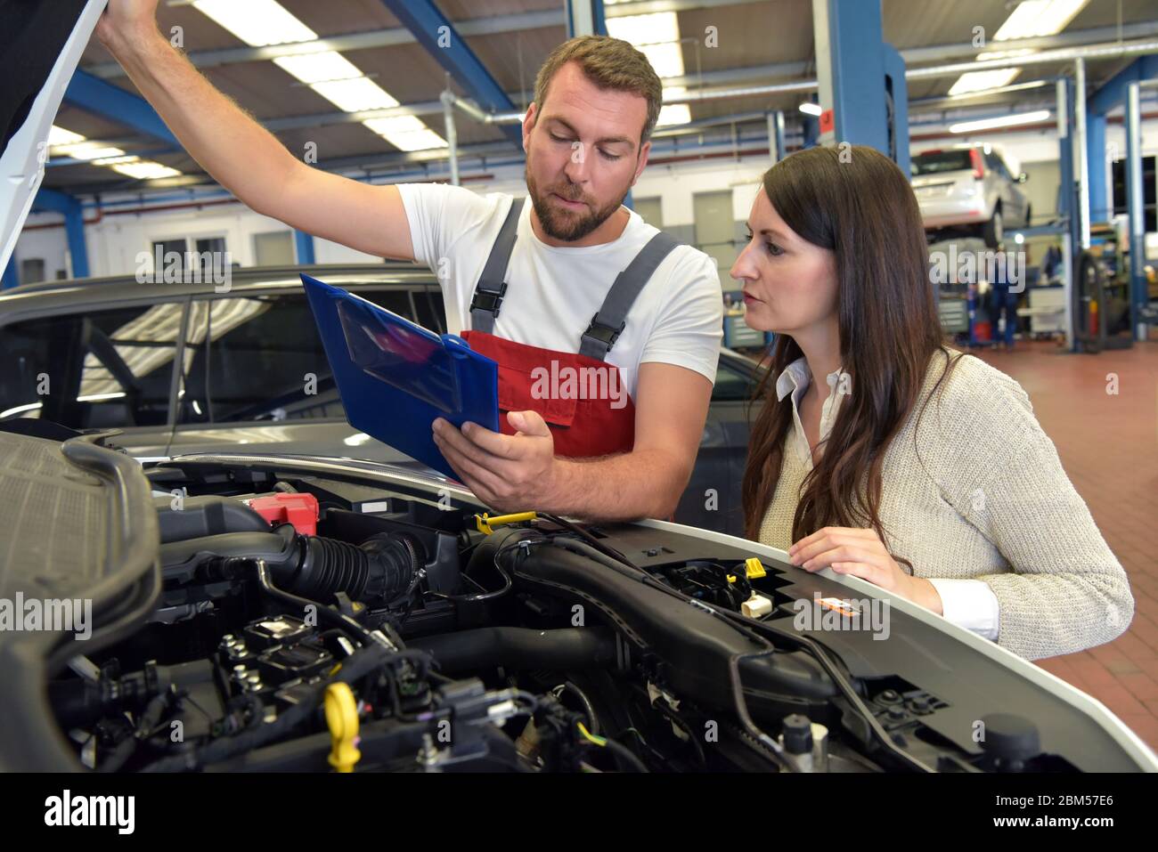 Service client : le mécanicien automobile et le client discutent de la réparation d'un véhicule sur site Banque D'Images