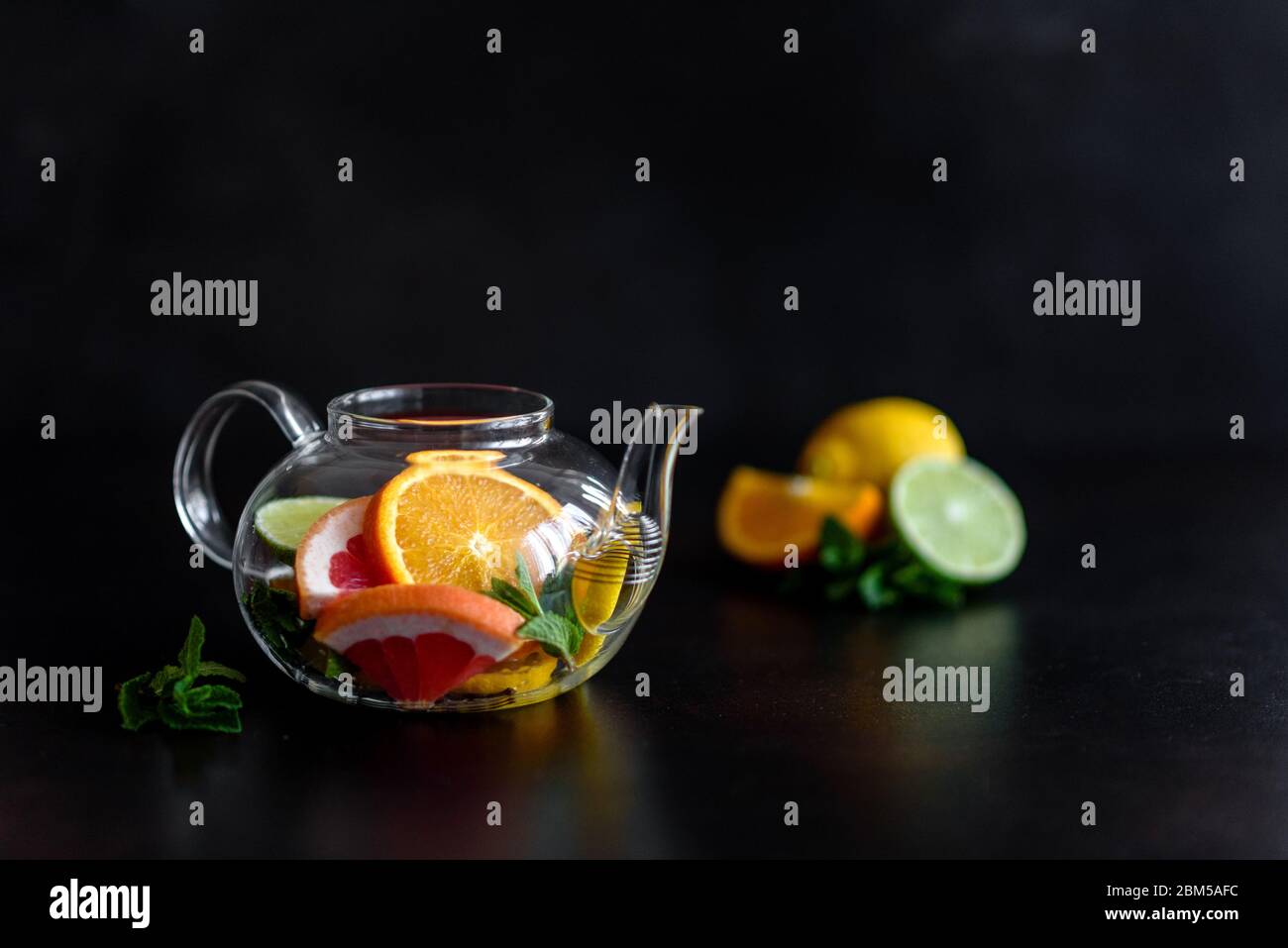 Thé chaud aux fruits avec citron, menthe, orange, citron vert et pamplemousse dans une belle théière en verre Banque D'Images