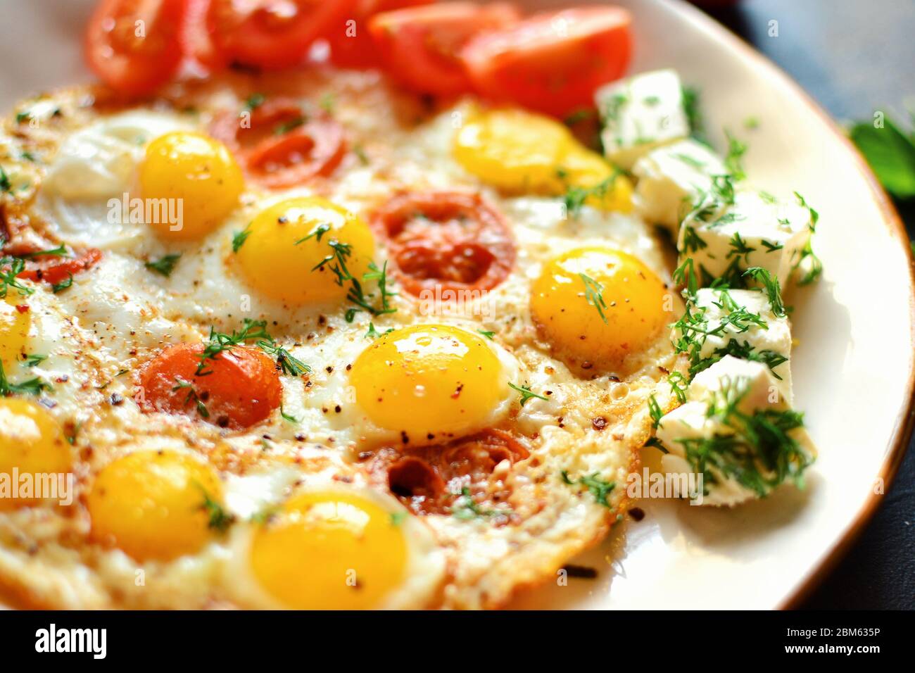 Œufs de caille frits dans une belle assiette sur fond de table sombre. Œufs frits avec tomates et aneth. Petit déjeuner savoureux et sain. Gros plan. Œufs frits Banque D'Images