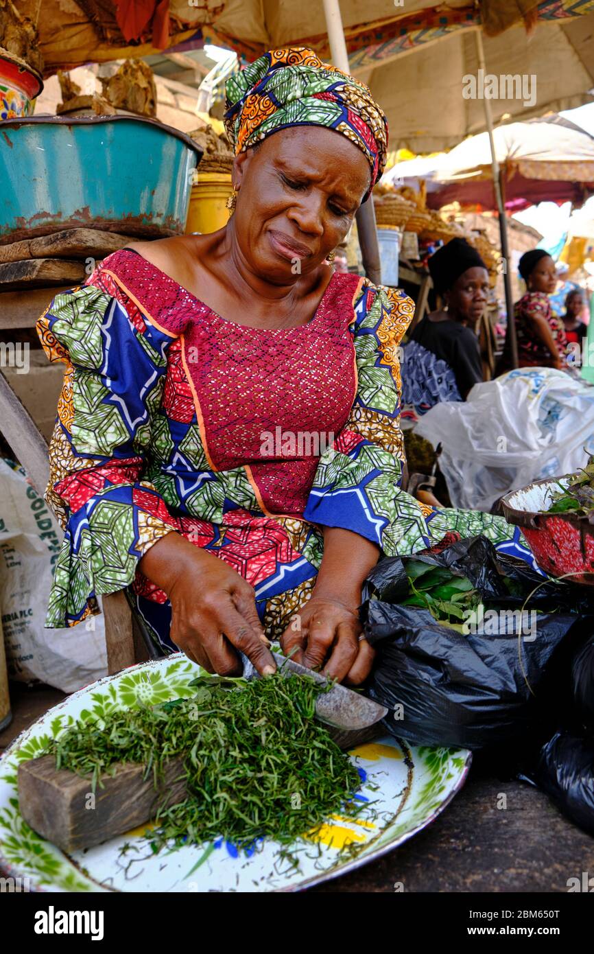 Femme vêtue de costume africain coloré coupant des légumes au marché d'Ilorin. Banque D'Images