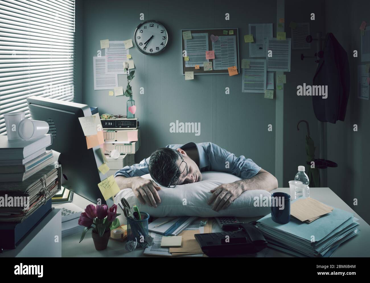 Homme d'affaires épuisé dormant au travail avec un oreiller sur son bureau. Banque D'Images