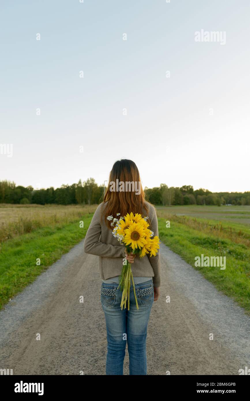 Vue arrière de la jeune femme asiatique tenant des tournesols derrière le dos dans la nature Banque D'Images