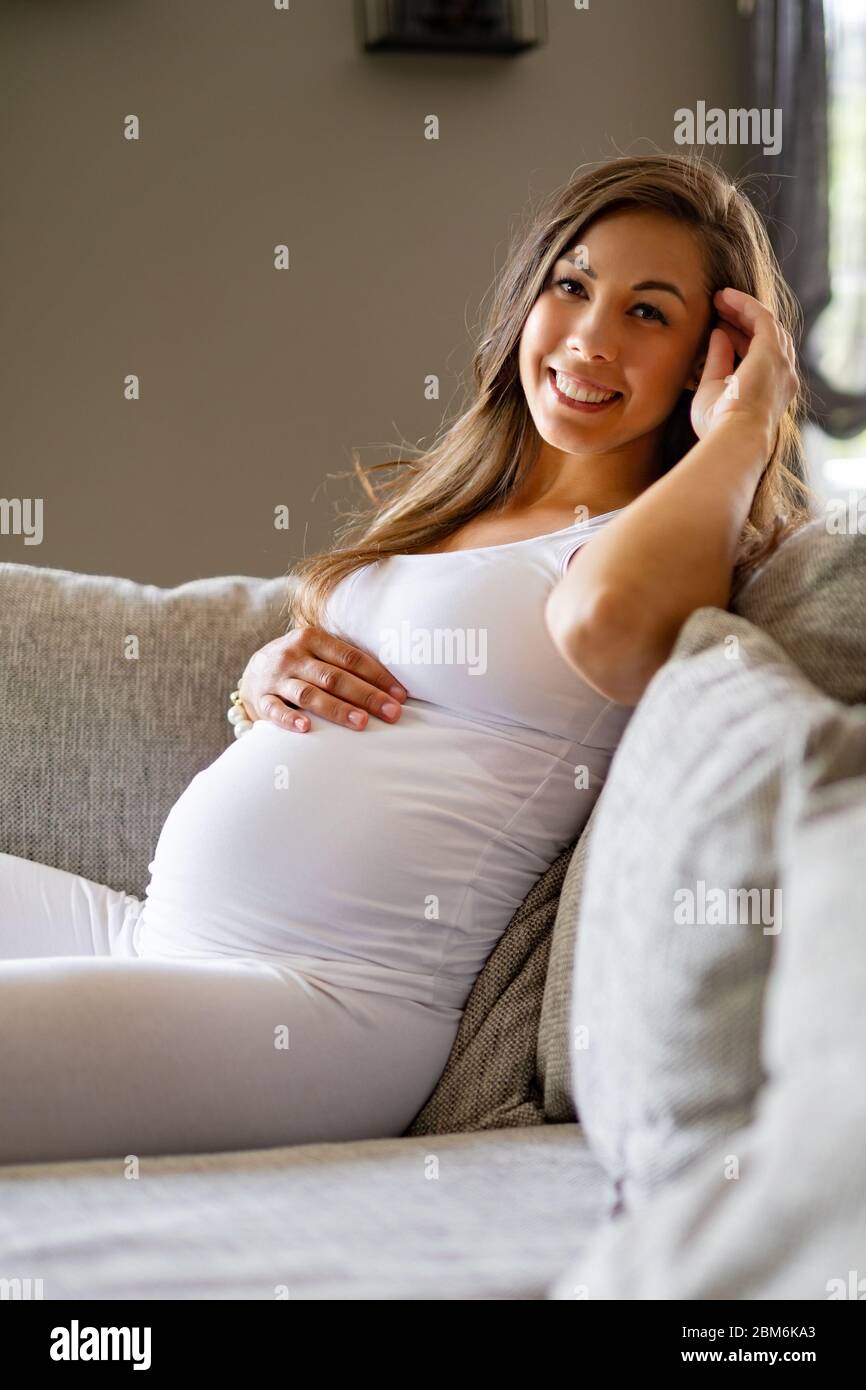 Bonne belle femme enceinte assise dans un canapé touchant son ventre Banque D'Images