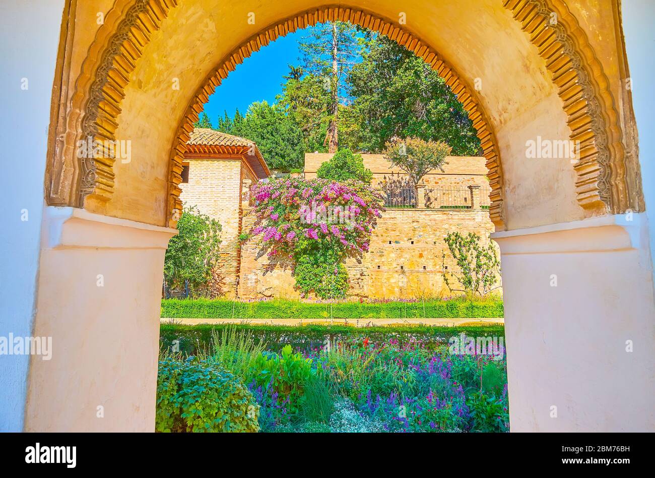 L'arche de style mudejar sculptée ouvre la vue sur les fleurs colorées et la végétation luxuriante du patio de l'irrigation de la Sorcière, Generalife, Alhambra, Grenade, Espagne Banque D'Images