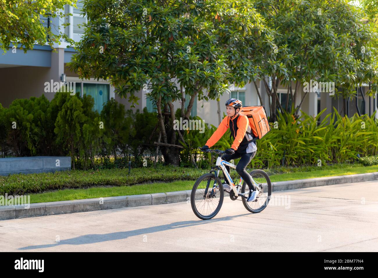 Un homme asiatique livrant à vélo des repas dans les rues de la ville avec une livraison de nourriture chaude des plats à emporter et des restaurants à la maison, livraison express de nourriture a Banque D'Images