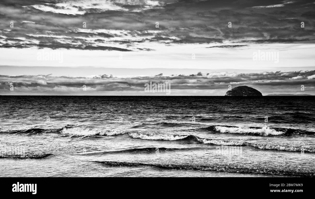Image en noir et blanc comme la marée tourne doucement les vagues se brisant, à l'horizon Ailsa Craig, nuages sombres spectaculaires, île écossaise, Écosse. Banque D'Images