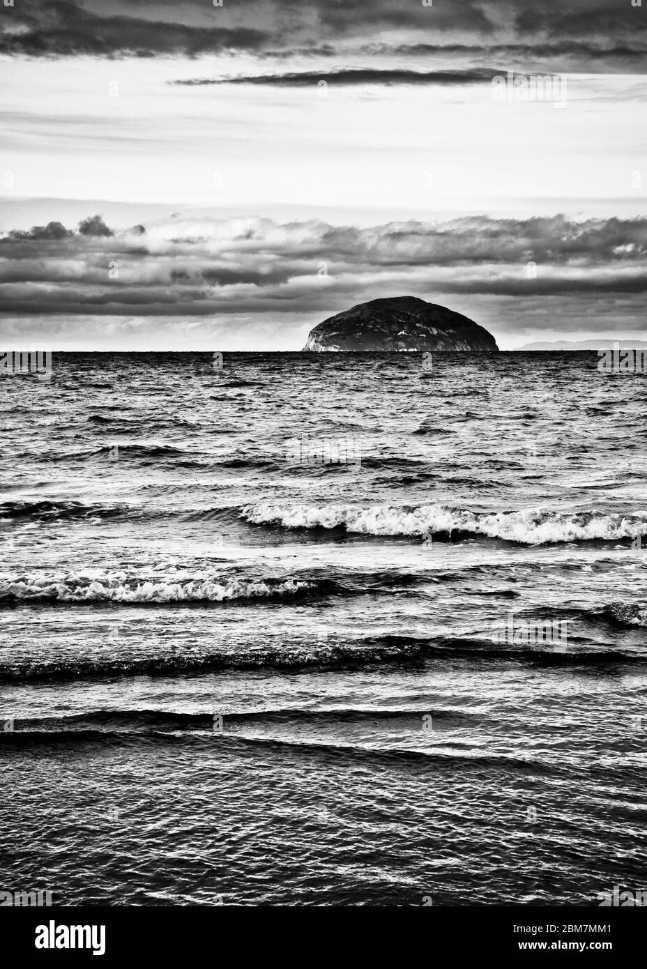 Image en noir et blanc comme la marée tourne doucement les vagues se brisant, à l'horizon Ailsa Craig, nuages sombres spectaculaires, île écossaise, Écosse. Banque D'Images