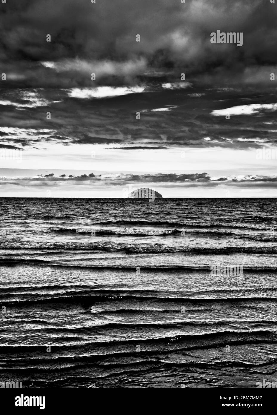 Image en noir et blanc comme la marée tourne doucement les vagues se brisant, à l'horizon Ailsa Craig, nuages sombres spectaculaires, île écossaise, Écosse. Banque D'Images