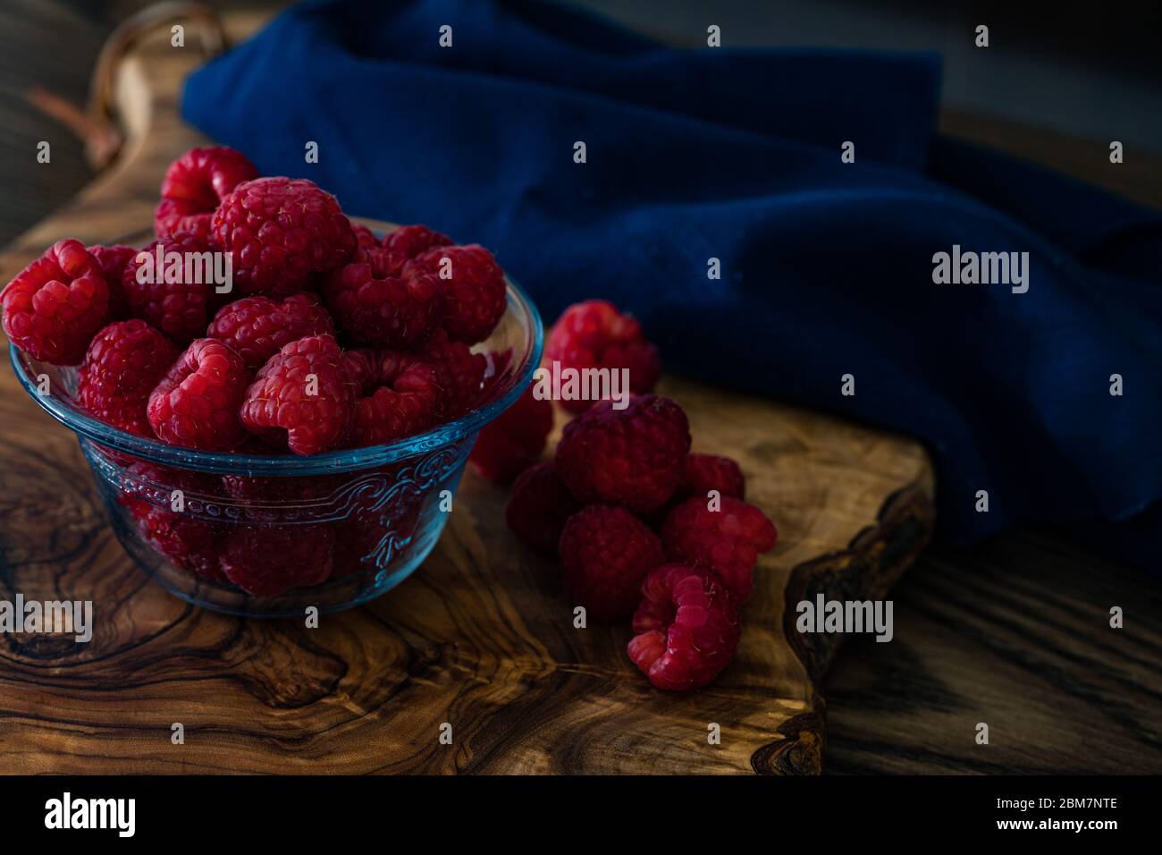 framboises dans un petit plat en verre sur une planche à découper en bois, éclairage de gros plan à faible intensité Banque D'Images