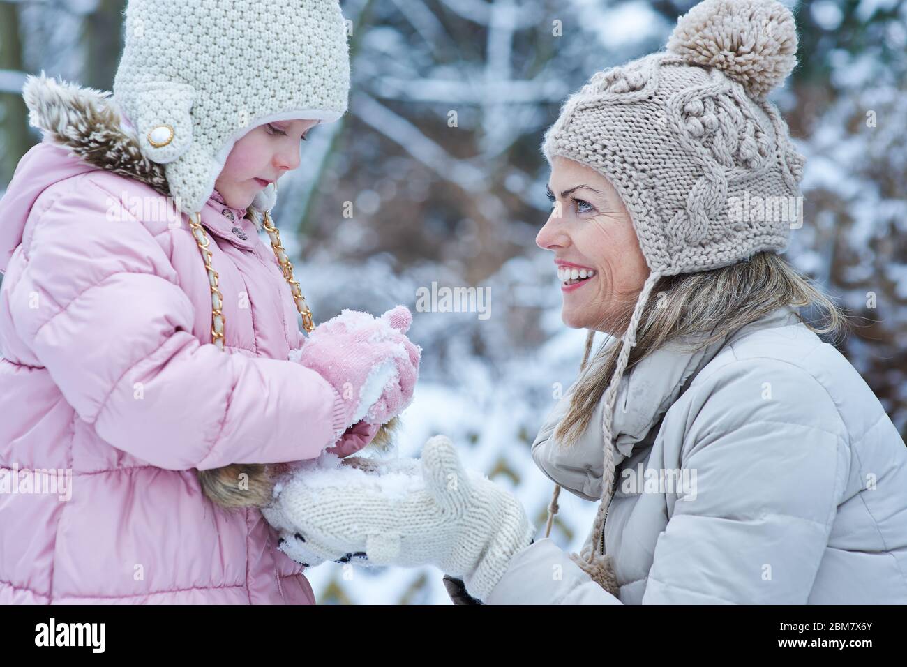 L'enfant construit un bonhomme de neige en hiver avec une mère qui rit Banque D'Images