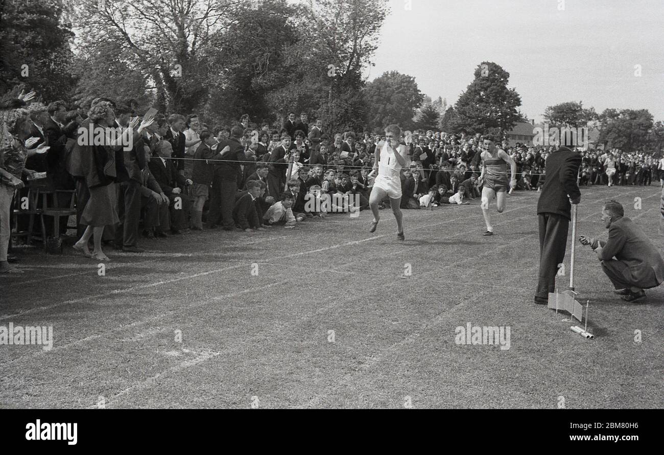 Sports d'école secondaire, Angleterre, c1960, dehors sur une piste de gazon, applaudi par une grande foule d'élèves et d'enseignants de l'école secondaire, deux jeunes hommes courant dur pour la bande d'arrivée à la fin d'une course de relais. Banque D'Images