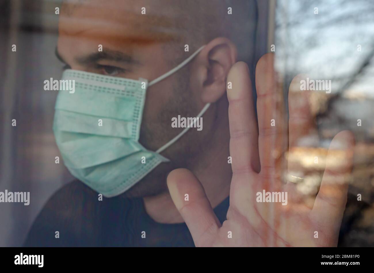 Homme caucasien infecté regardant par la fenêtre dans le masque protecteur. Concept d'auto-isolation. Banque D'Images