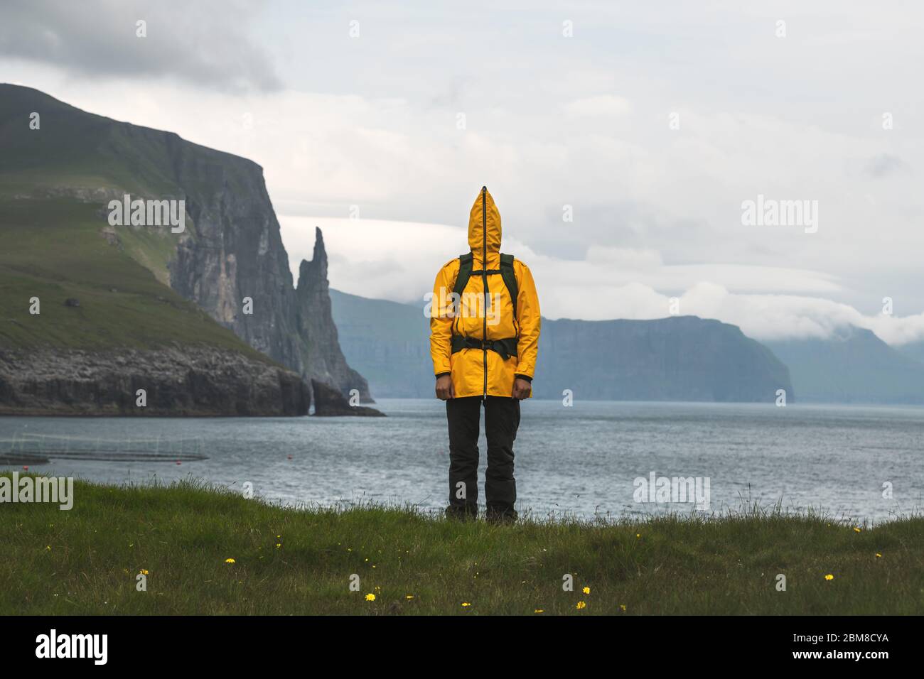 Touriste dans une veste jaune drôle au point de vue de Trollkonufingur près des falaises de Witches Finger. Île de Vagar, îles Féroé, Danemark. Banque D'Images