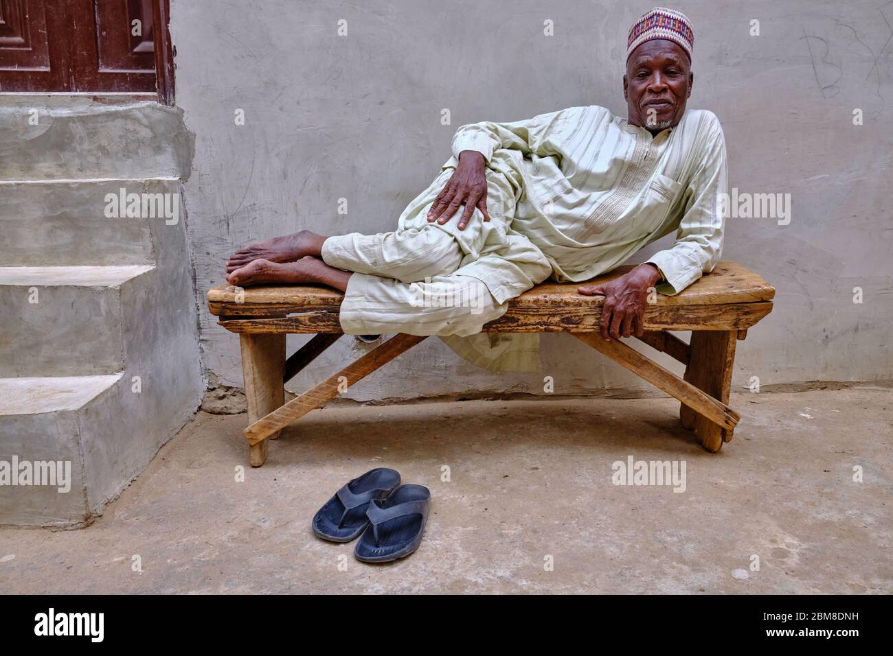 Portrait d'un homme nigérian d'âge moyen allongé sur un banc en bois. Banque D'Images