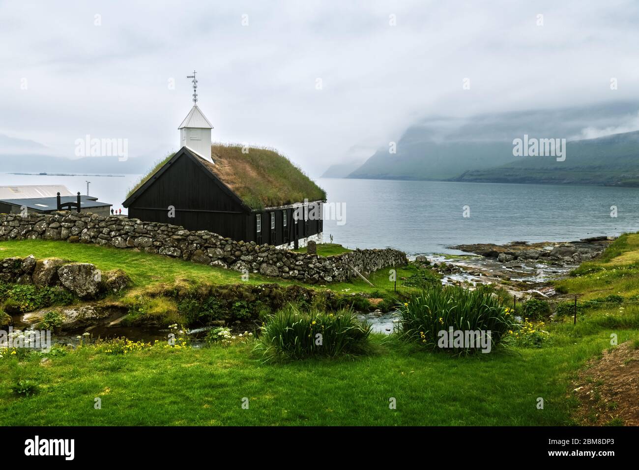 Vue d'été sur l'église traditionnelle au sommet d'un gazon dans le village de faroese. Paysage de beauté avec fjord de brouillard et hautes montagnes. Île de Strymoy, îles Féroé, Danemark. Banque D'Images