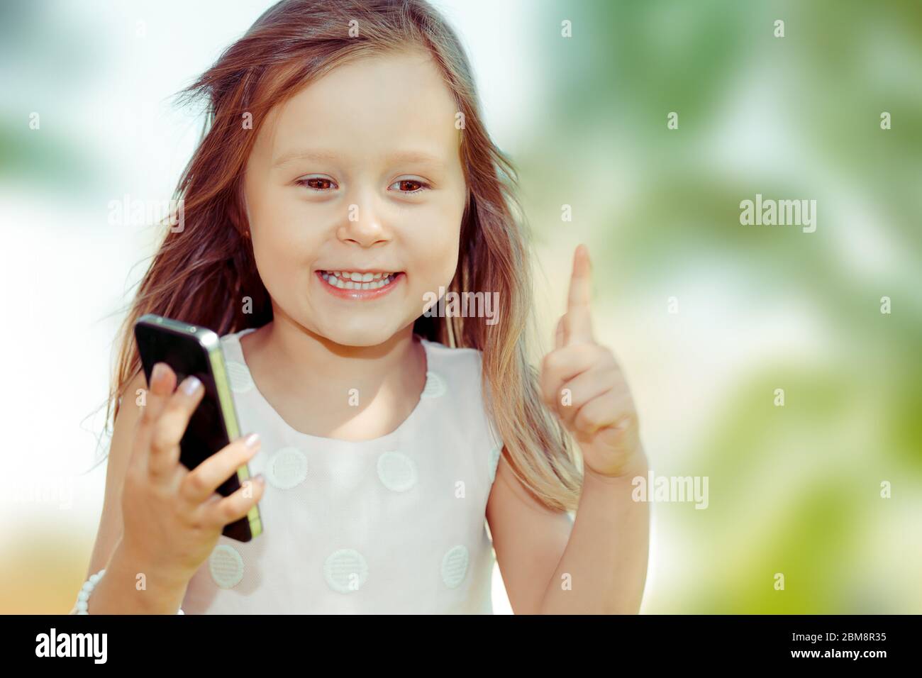 Enfant avec smartphone. Gros plan portrait de jolie fille enfant tenant le téléphone cellulaire montrant non, ne pas, attention avec le doigt de geste de main. Blocage dangereux Banque D'Images