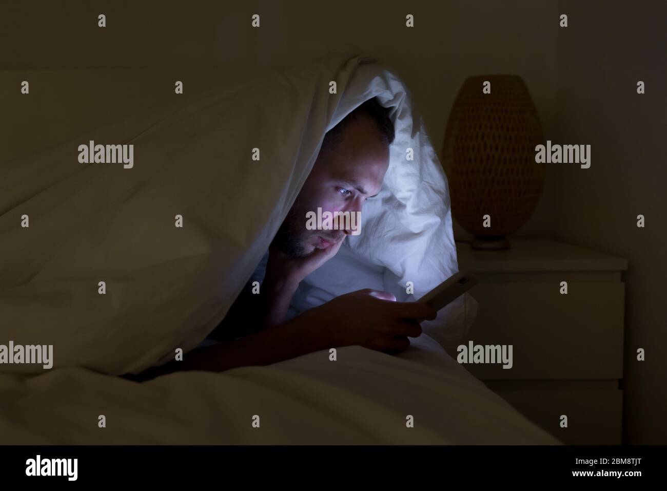 Dépendance mobile, nomophobie, insomnie, concept de trouble du sommeil. Homme ennuyé à discuter et surfer sur Internet avec smartphone tard dans la nuit, allongé sur être Banque D'Images