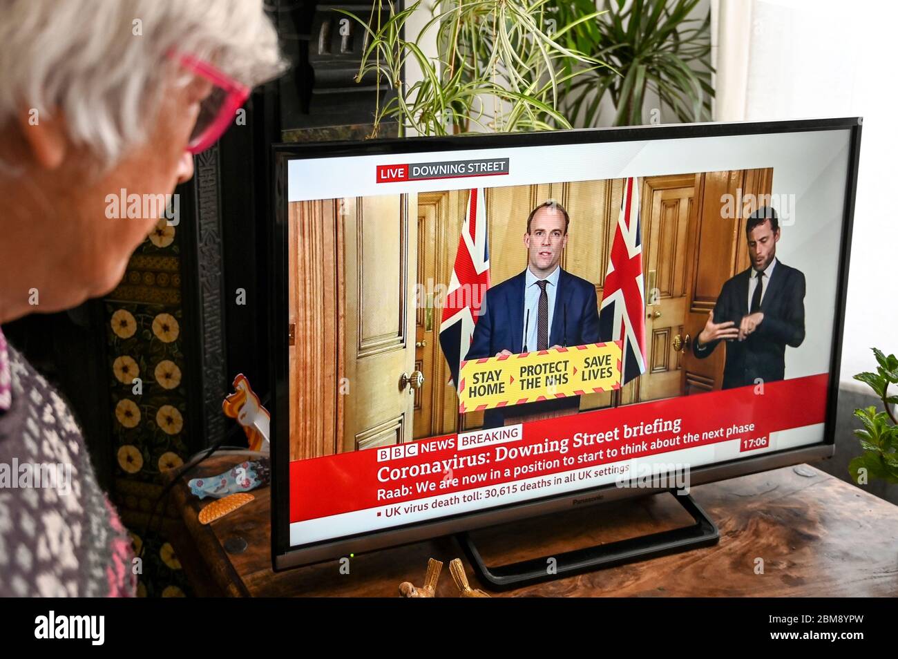 Dominic Raab donne le briefing quotidien télévisé du coronavirus Downing Street, regardé par un spectateur. Bannière « domicile, protéger le NHS, sauver des vies ». Banque D'Images