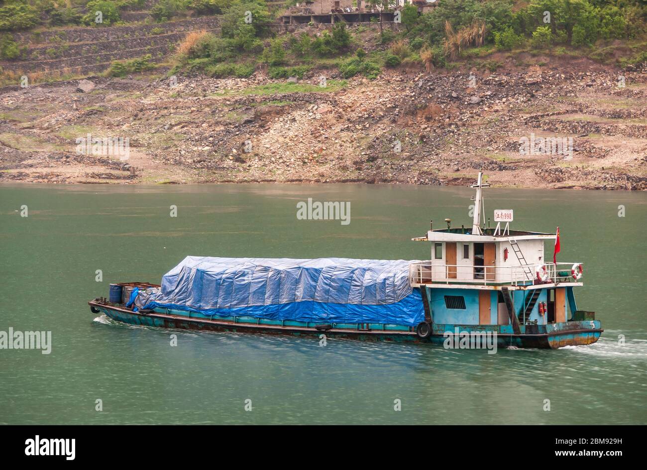 Xiangxicun, Chine - 6 mai 2010 : gorge de Xiling sur le fleuve Yangtze. Gros plan de la petite barge avec charge recouverte de bâche bleue sur l'eau verte. Pierre brune et Banque D'Images