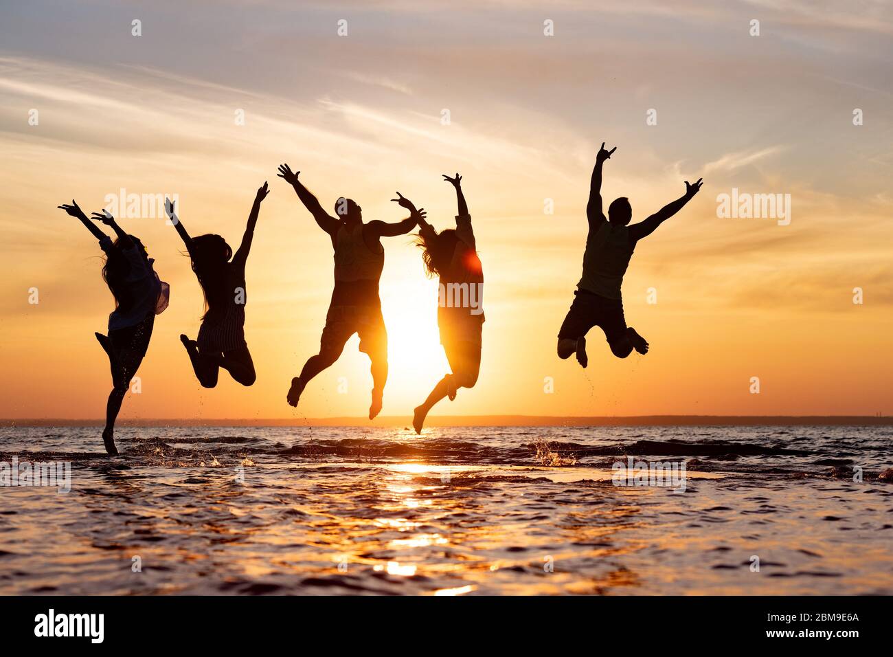Cinq amis heureux s'amusent et sautent sur la plage du coucher du soleil Banque D'Images