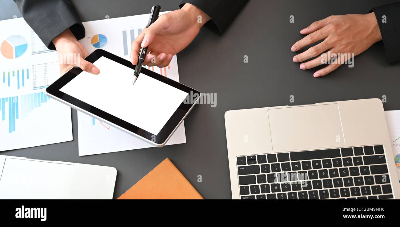 Image rognée des professionnels travaillant avec une tablette, un ordinateur portable et des graphiques tout en étant assis à une table de réunion noire au-dessus de M. Banque D'Images