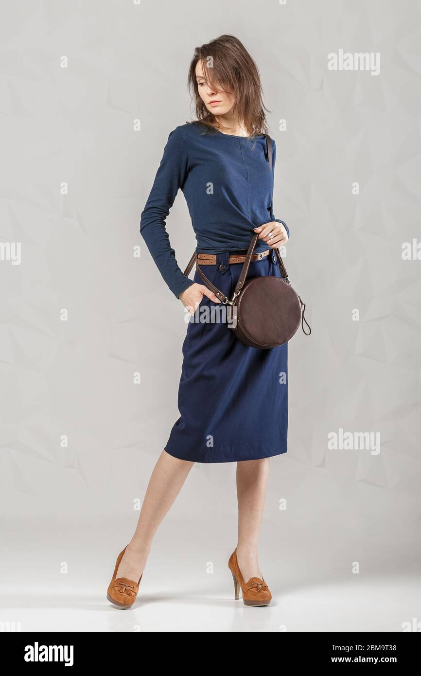 Femme élégante et tendance portant une manches longues bleu classique, une jupe  et des talons bruns tenant un sac à main rond en cuir tendance. Vêtements et  accessoires. F Photo Stock -