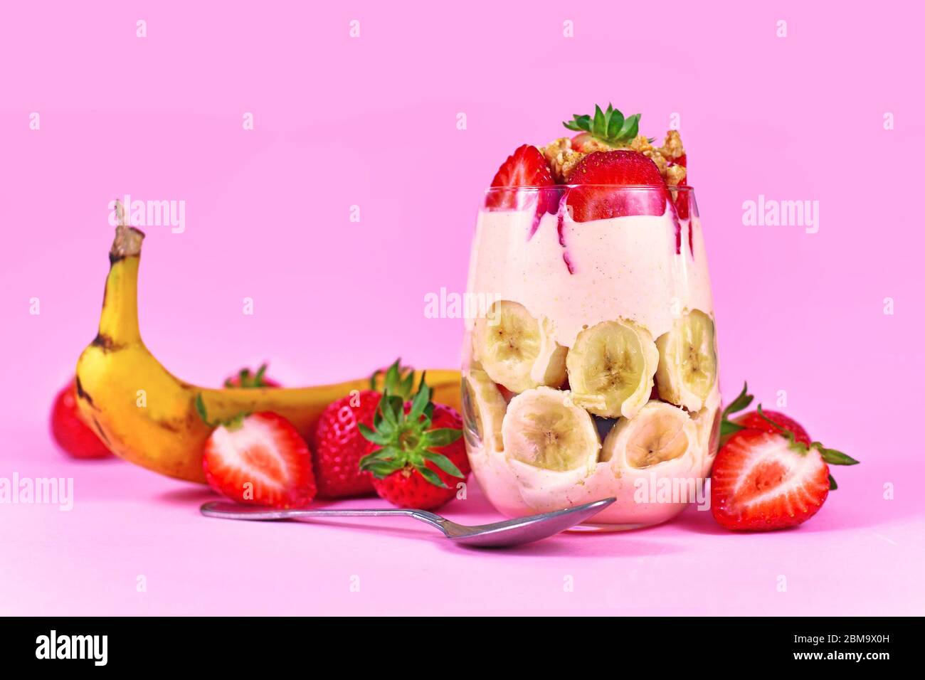 Dessert d'été sain aux fruits de la banane et de la fraise avec yaourt et granola sur fond rose Banque D'Images
