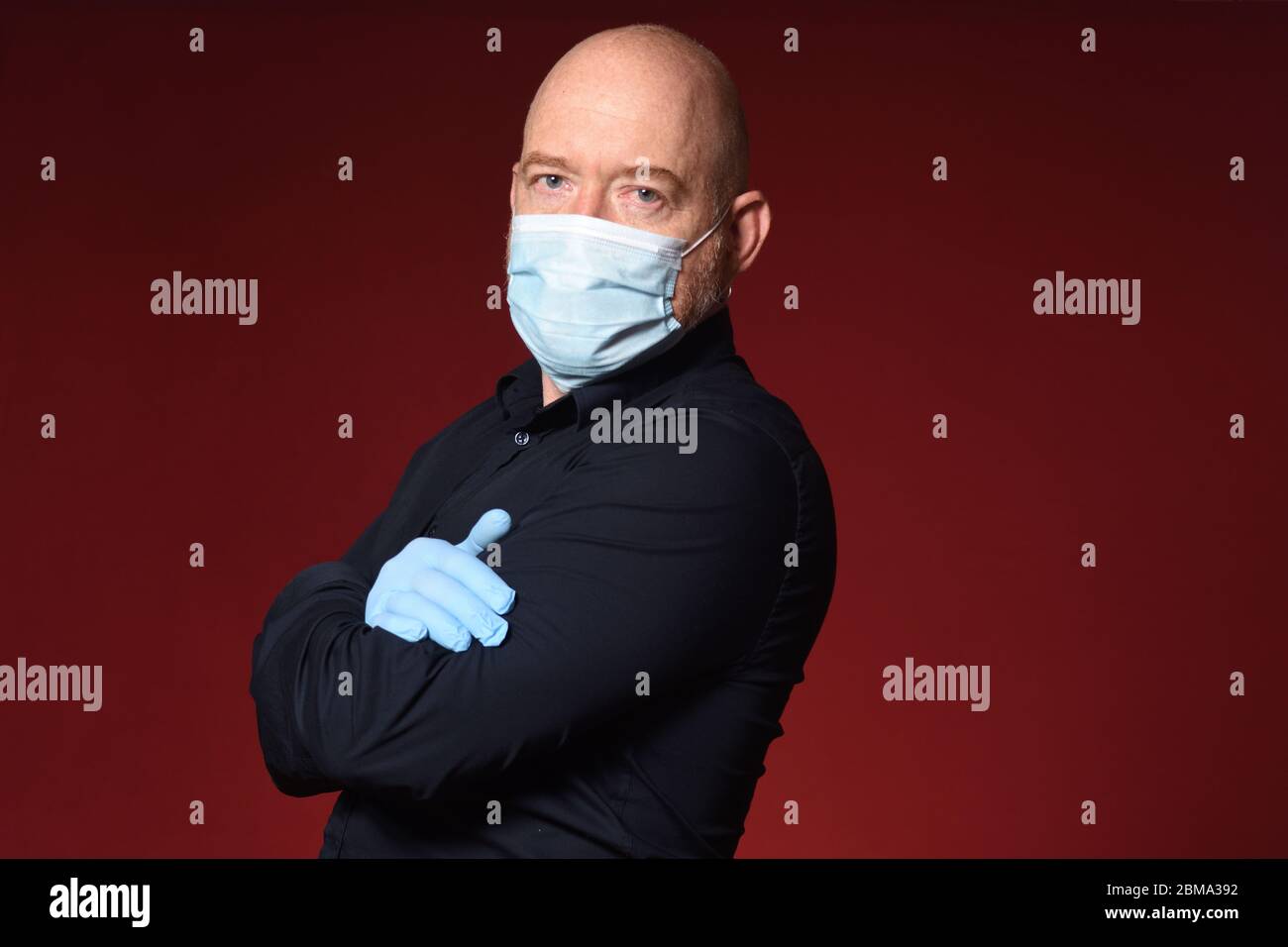 portrait d'un homme avec des gants et des bras de masque croisés sur un fond rouge Banque D'Images