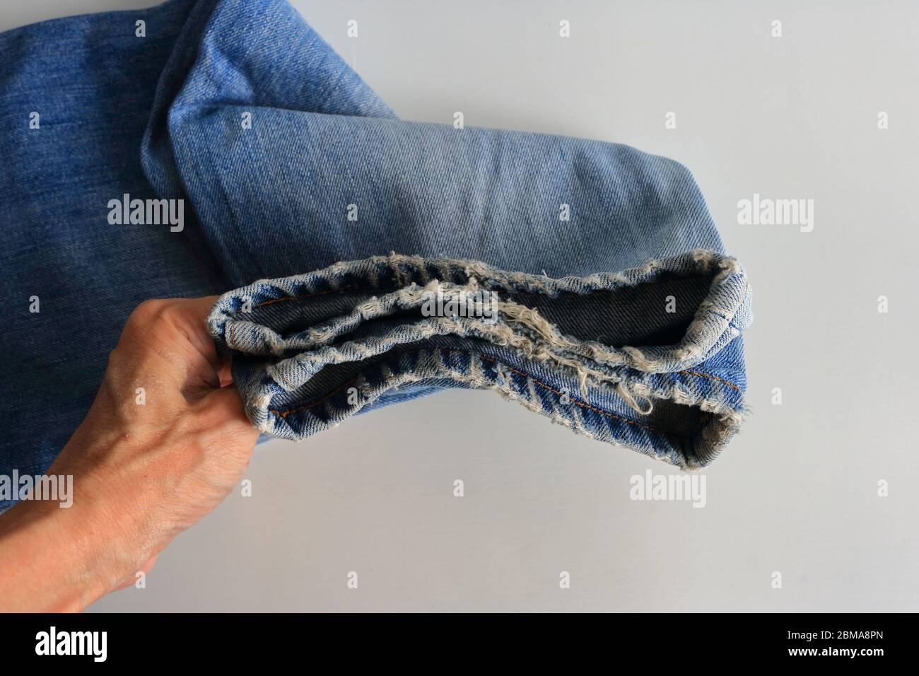 Main tenant les jambes effilochées d'une paire de jeans placés sur une table blanche, mise au point sélective Banque D'Images