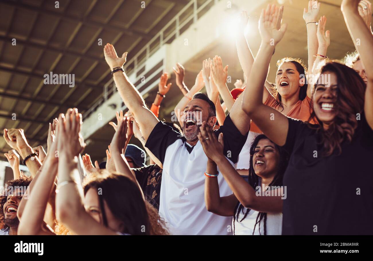 Une foule de fans de sport applaudissent lors d'un match dans le stade. Des personnes enthousiastes debout avec leurs bras levés, applaudissant et hurant pour encourager leur équipe. Banque D'Images