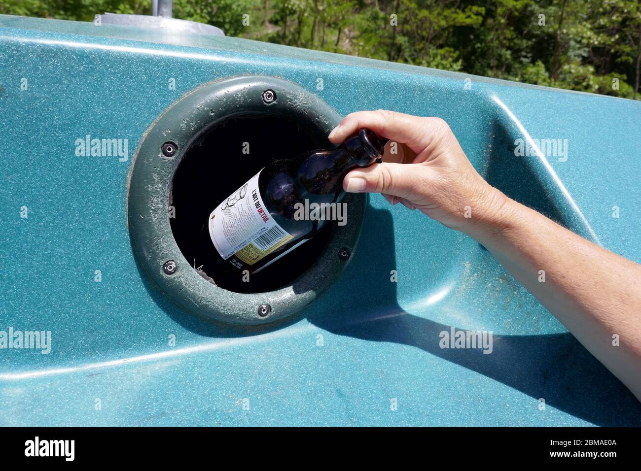Bouteille en verre avec main femelle placée dans un grand bac de recyclage en plastique dans la région d'Ariège, dans le sud de la France Banque D'Images