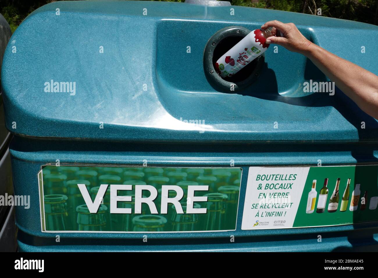 Bouteille en verre avec main femelle placée dans un grand bac de recyclage en plastique dans la région d'Ariège, dans le sud de la France Banque D'Images