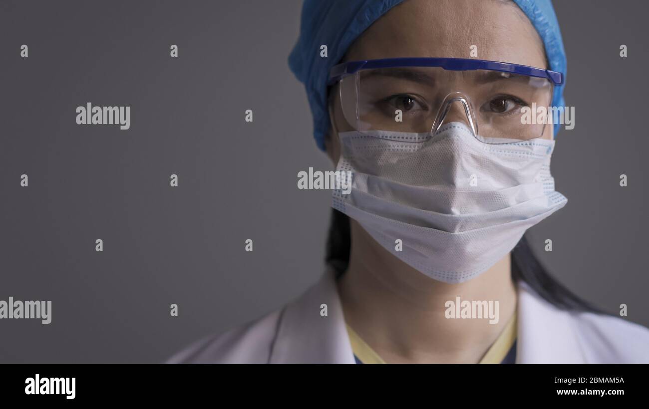 Femme inquiète médecin regardant l'appareil photo portant un uniforme médical de protection, un masque, un capuchon et des lunettes. Une infirmière asiatique se sente stressante pendant une pandémie. Fermer Banque D'Images