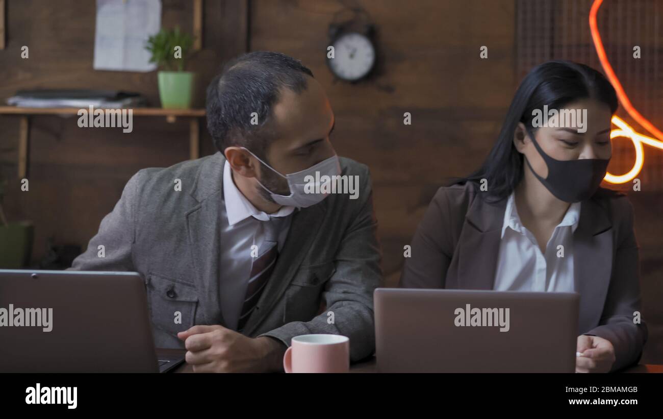Discussion avec l'équipe Entreprises. L'homme et la femme dans des masques protecteurs communiquent assis à un bureau moderne pendant une épidémie de coronavirus Banque D'Images