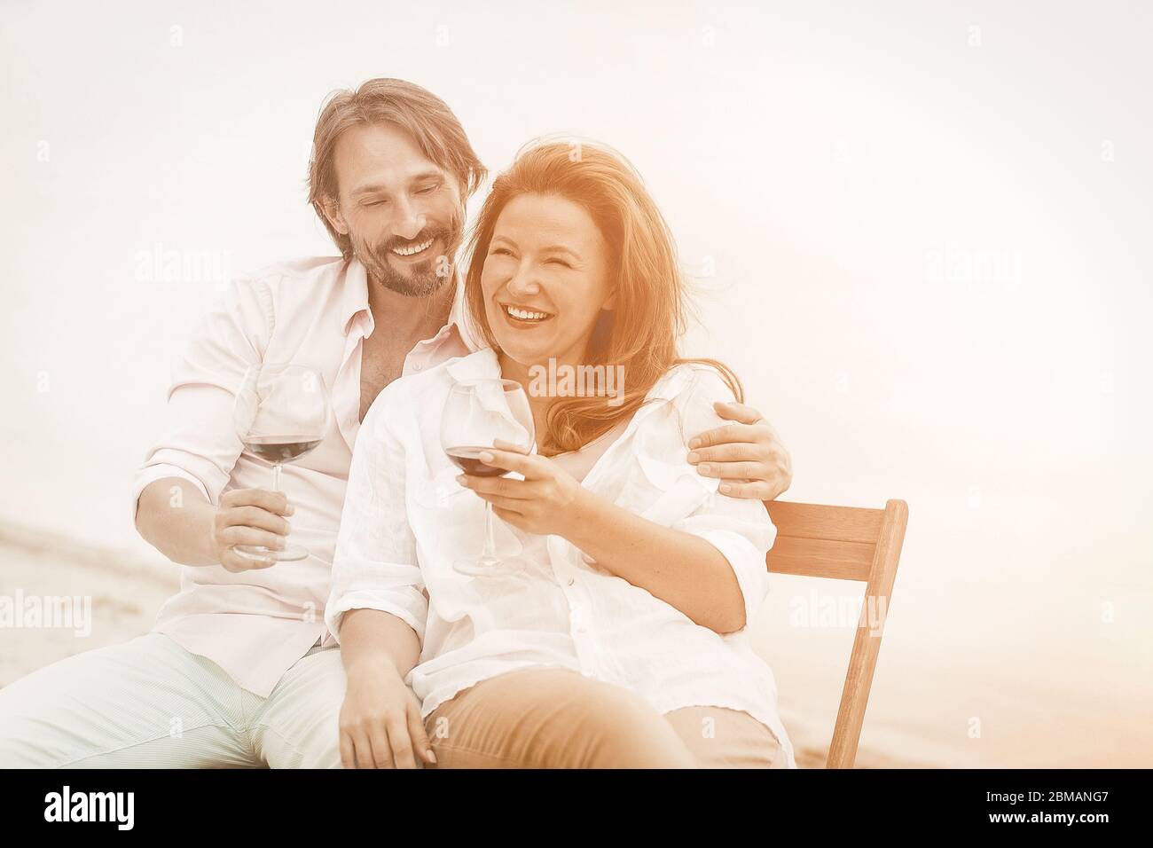Un couple heureux passe du temps à se reposer ensemble près de la mer. Homme et une femme boivent du vin rouge sourire et embrasser tout en s'asseyant près de l'eau à l'extérieur. Ton Banque D'Images