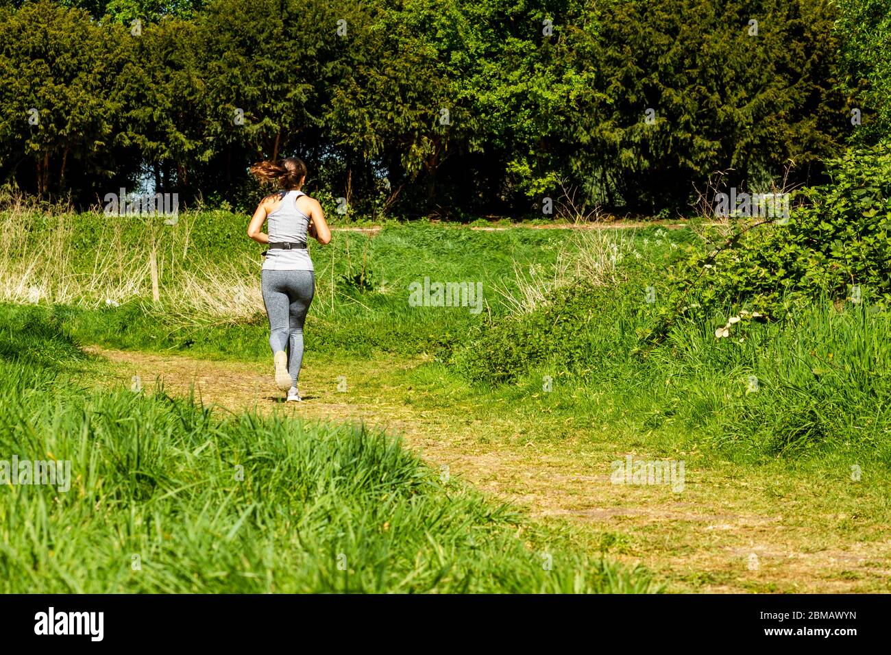 Femme qui fait du jogging sur un sentier vert dans les Hackney Marshes, Londres Banque D'Images