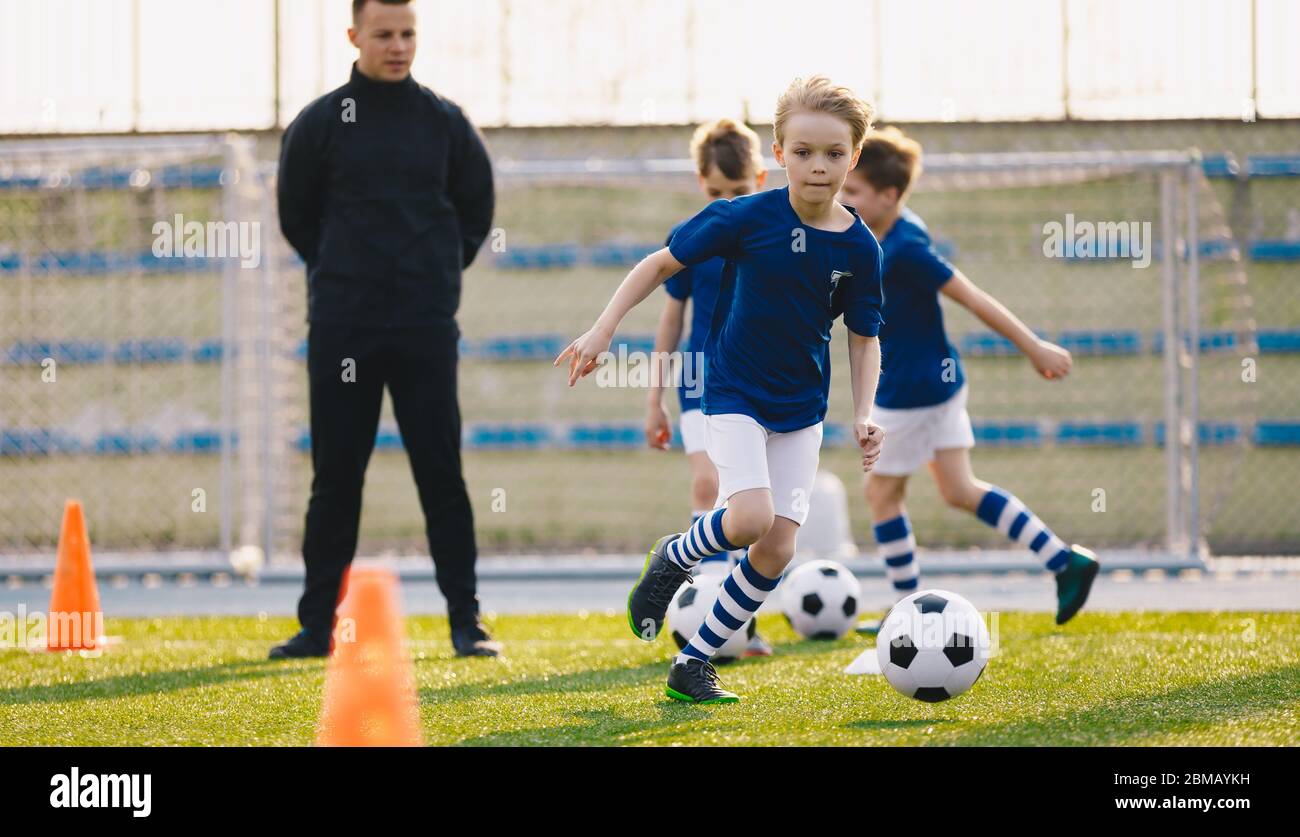 Joyeux garçon pratiquant le football sur le terrain. Un entraîneur de jeunes entraîneurs de football pour enfants sur les installations sportives scolaires Banque D'Images