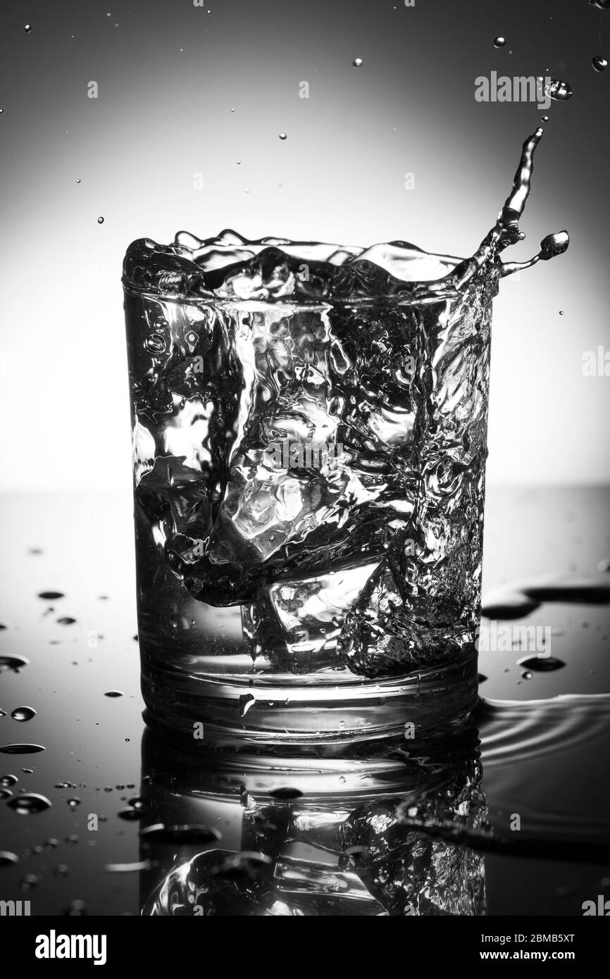 verre d'eau avec éclaboussures de la chute de glace cube, photographie noir et blanc . Banque D'Images
