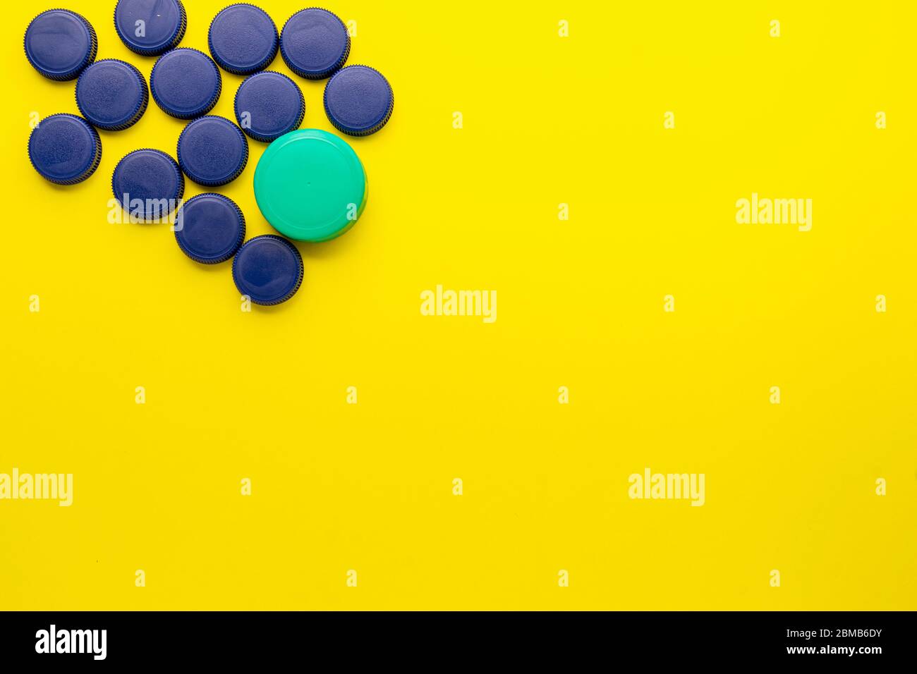Bouchons de bouteille en plastique situés dans le coin supérieur gauche sur fond jaune. Concept de recyclage dans le conteneur jaune. Banque D'Images