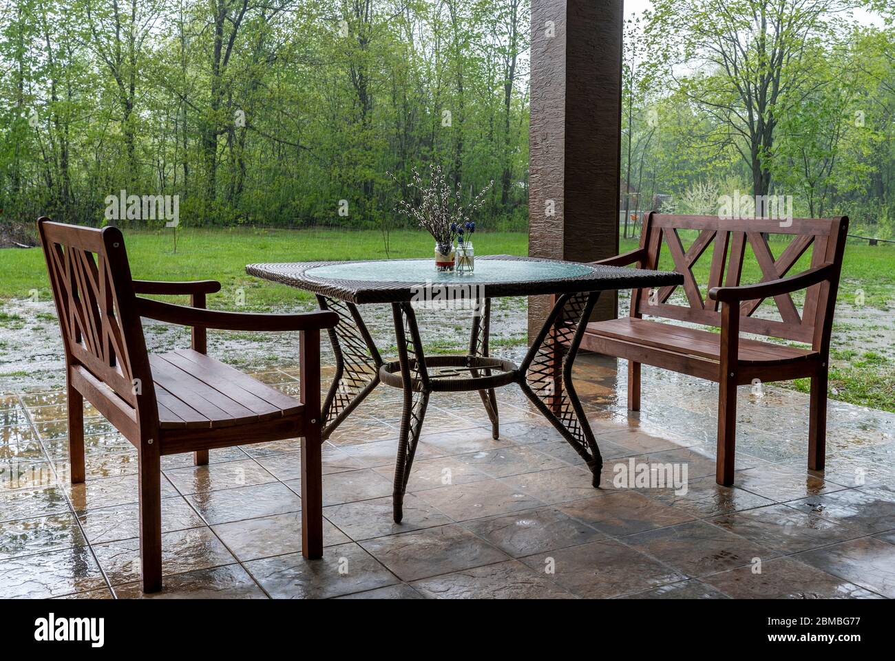 Deux bancs en bois et une table se tiennent sur la véranda extérieure sous une forte pluie. Banque D'Images