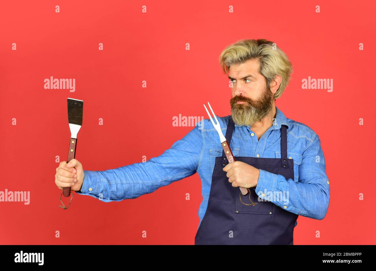 Outils pour rôtir la viande. Qui cuisinent mieux. Le défi ultime de la cuisine. Préparez le dîner pour la famille. Utilisez des ustensiles de cuisine et divers produits. Le chef mûr utilise des ustensiles de cuisine pour le barbecue. Banque D'Images