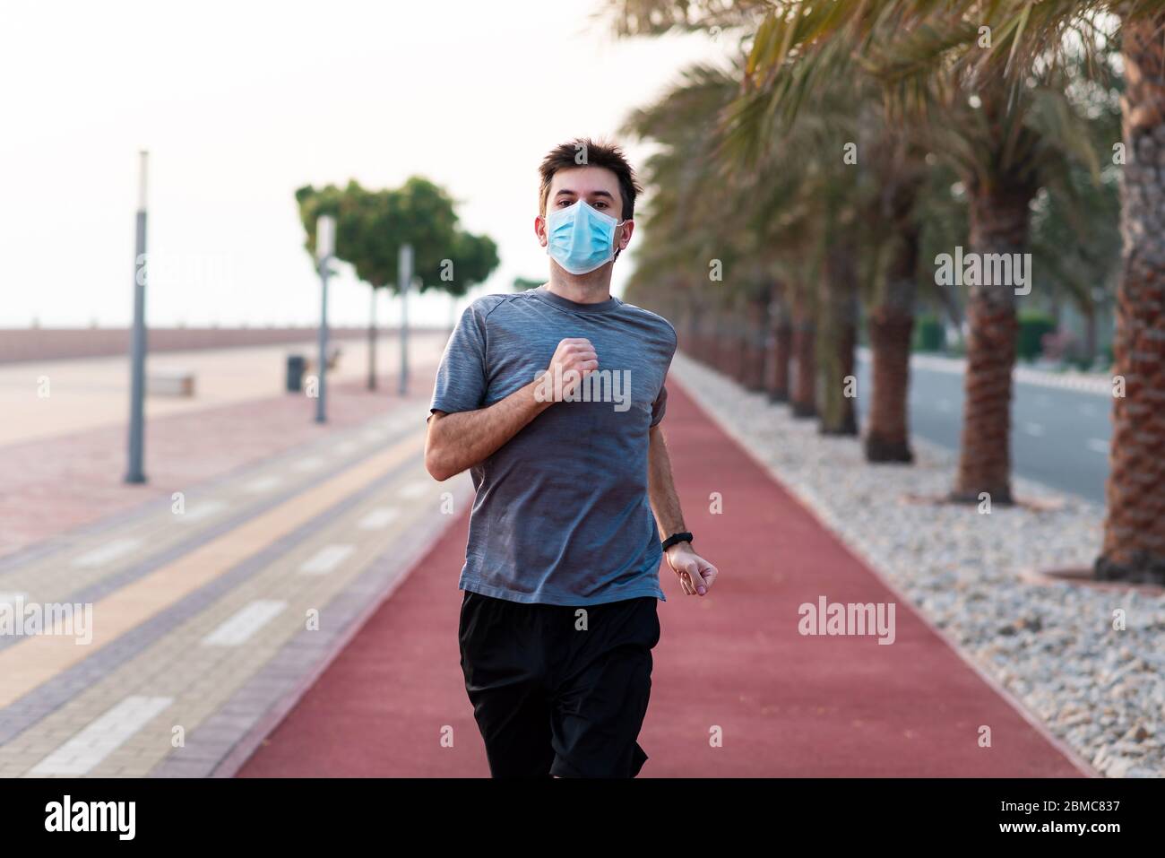 Homme qui fait du jogging sur la piste de course avec un masque chirurgical de protection Banque D'Images