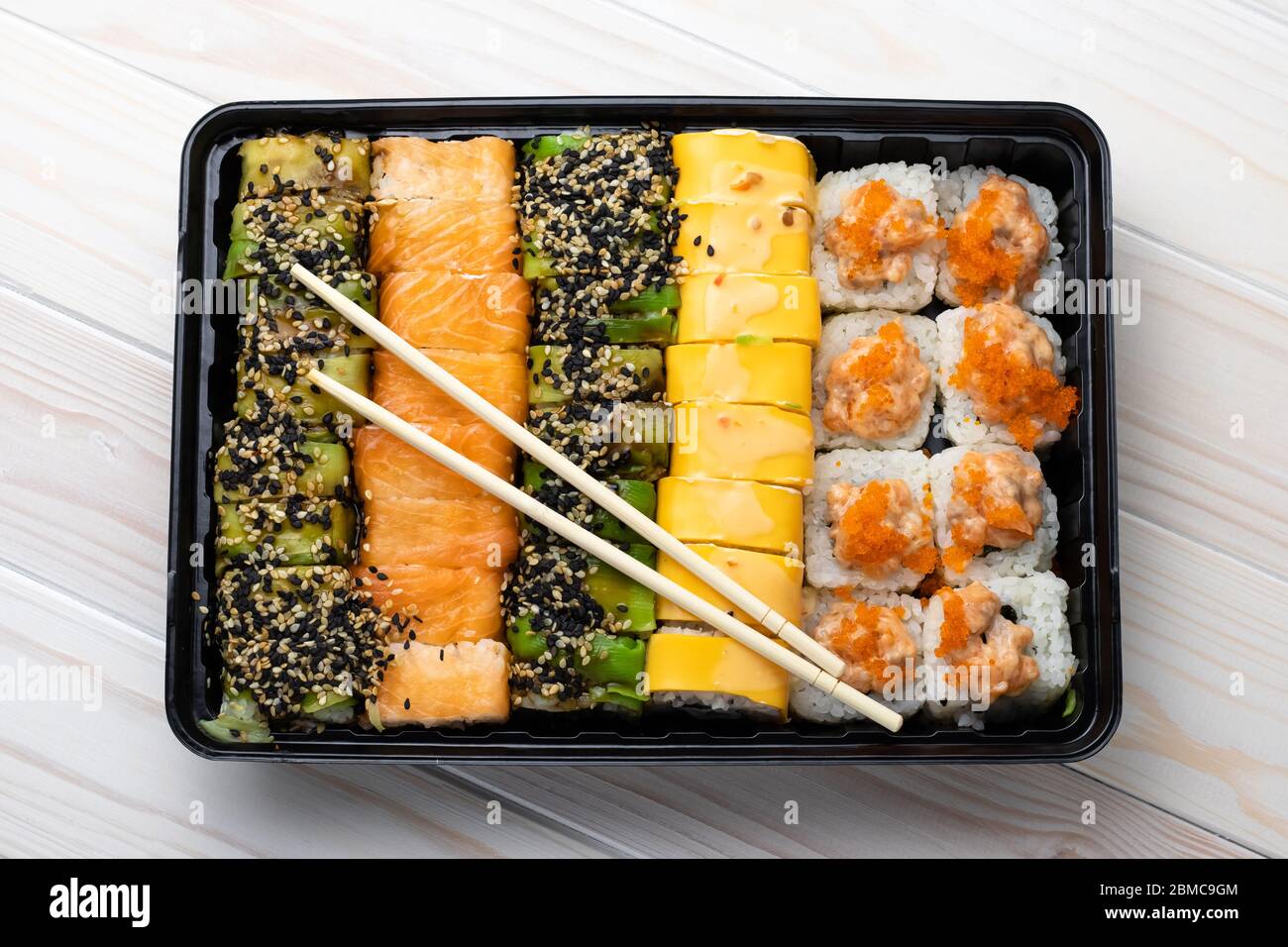 Ensemble de petits pains à sushis avec saumon et légumes sur plateau noir et baguettes en bois sur planches. Plats asiatiques de fruits de mer. Une cuisine japonaise traditionnelle Banque D'Images