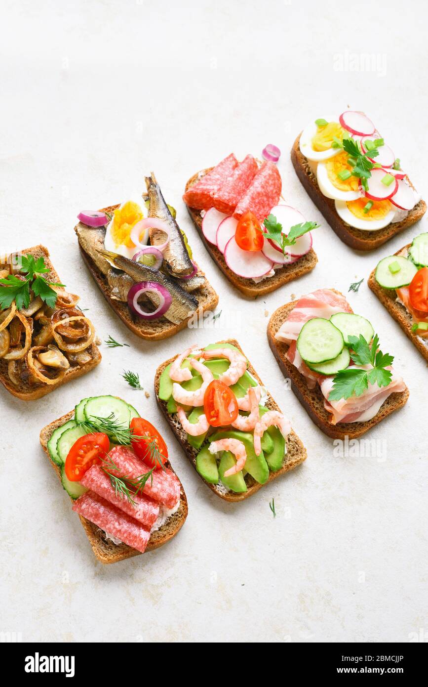 Ensemble de différents sandwiches avec viande, légumes, fruits de mer. Assortiment de sandwichs ouverts sur fond de pierre légère. En-cas savoureux et sains. Banque D'Images