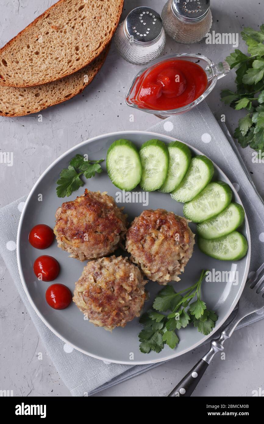 Côtelettes de bœuf servies avec une sauce au concombre et à la tomate sur une assiette grise sur fond de béton gris, format vertical Banque D'Images