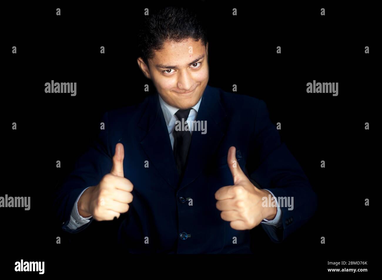 Portrait d'un jeune homme d'affaires souriant et charmant en chemise bleu foncé et souhaitant le meilleur des vœux de chance avec les pouces ou le geste de la main du meilleur de la chance Banque D'Images
