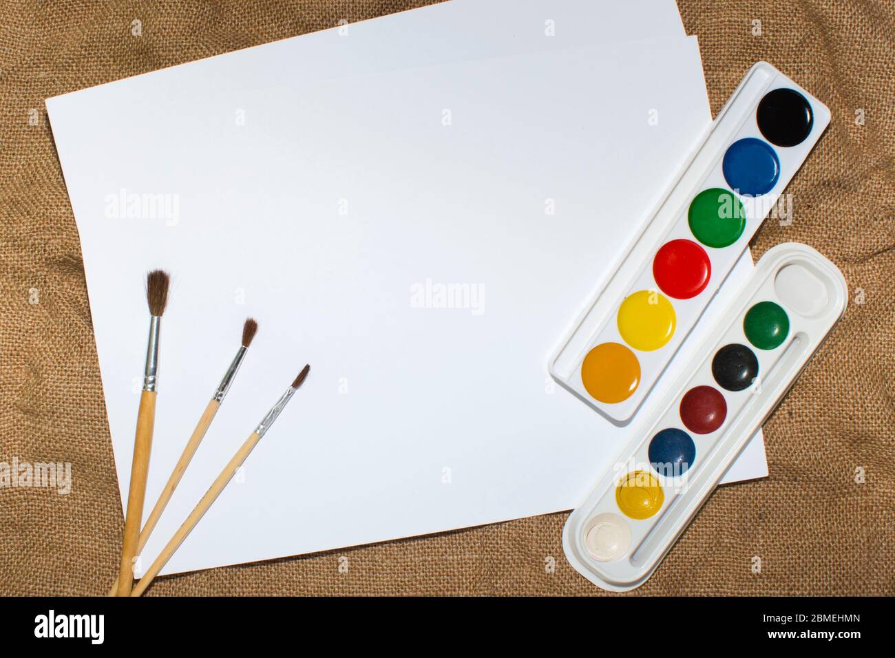 Ensemble de peintures aquarelles, pinceaux pour la peinture et feuille de papier blanc vierge de carnet d'esquisses. Vue de dessus. Banque D'Images