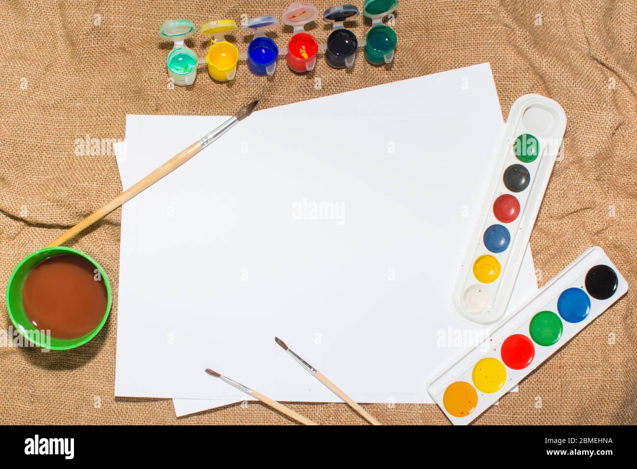 Ensemble de peintures aquarelles, pinceaux pour la peinture et feuille de papier blanc vierge de carnet d'esquisses. Vue de dessus. Banque D'Images