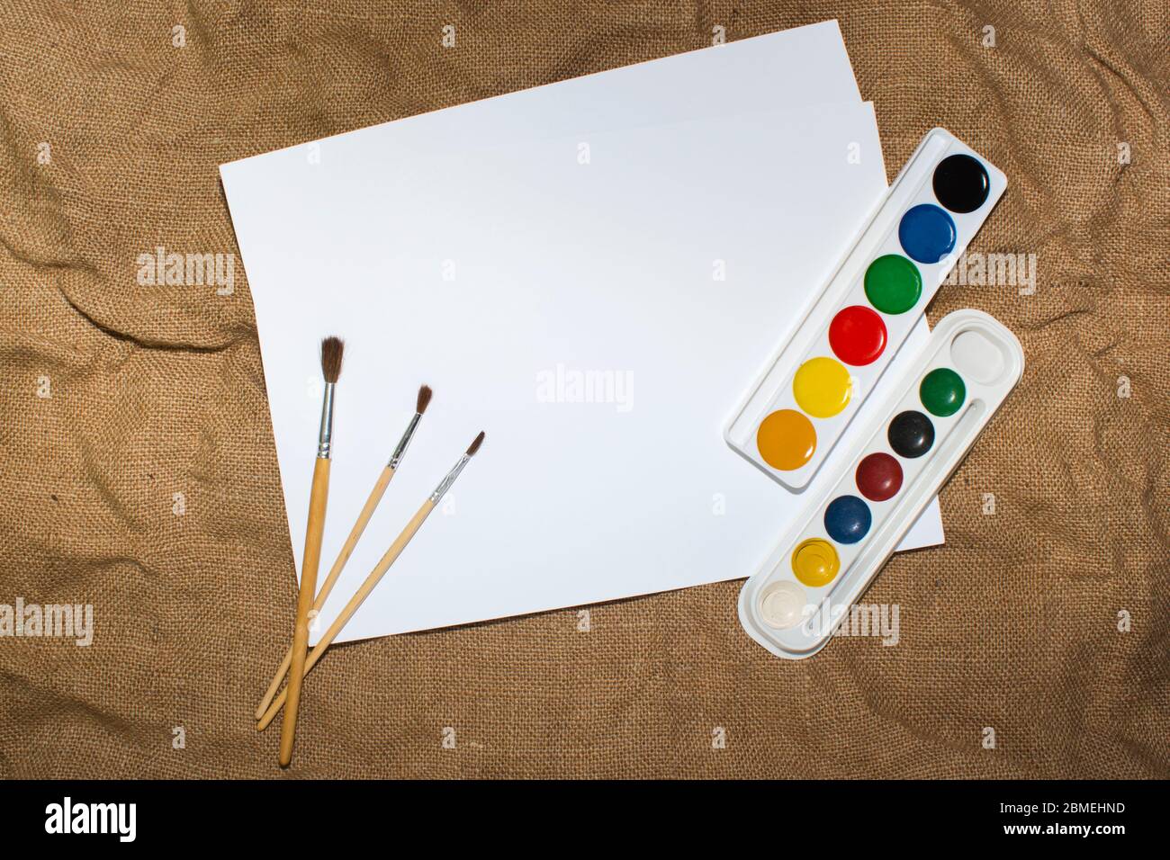 Ensemble de peintures aquarelles, pinceaux pour la peinture et feuille de papier blanc vierge de carnet d'esquisses. Vue de dessus. Banque D'Images