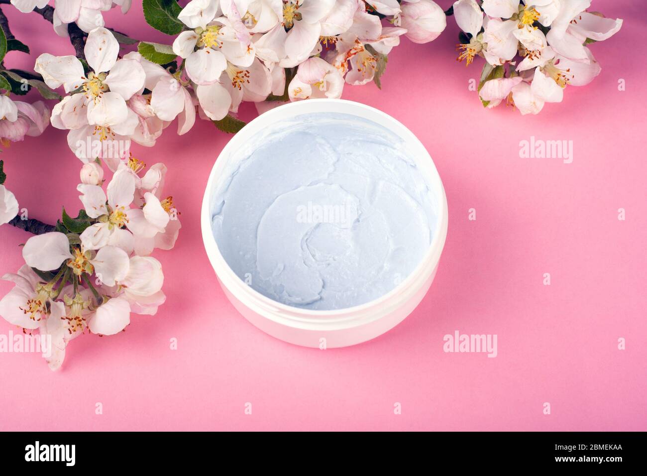 gommage corporel aux fleurs blanches de pomme sur fond rose, soins de la peau, spa, beauté. Banque D'Images